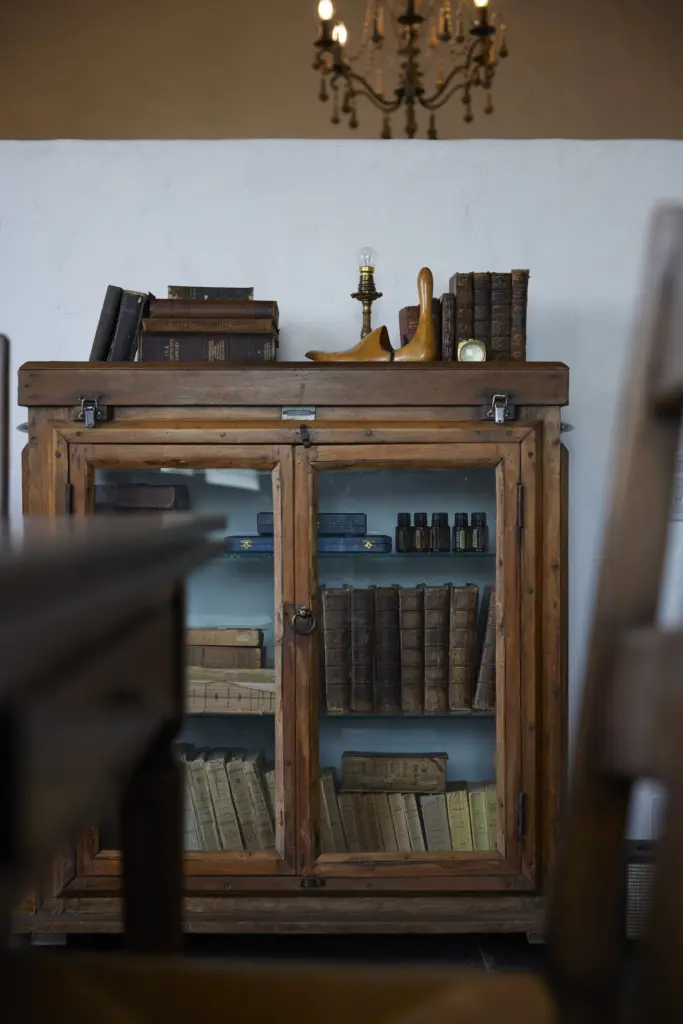 白い漆喰調の壁を背景に配置された、古い洋書やアンティーク小物がディスプレイされている木製のガラスキャビネット。アンティクのモデルハウスの、世界観を創り出すこだわりのインテリア家具