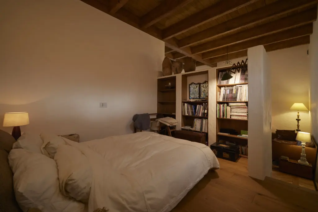 板張りの天井と無垢材の床が心地よい、アンティクのモデルハウスの寝室。白い漆喰調の間仕切り壁を活用した天井まである造作本棚やステンドグラス、温かな光を放つアンティークランプが、落ち着きのあるリラックス空間を演出している