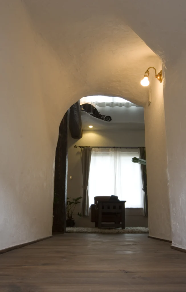 白い漆喰調の美しいアーチ壁で緩やかに仕切られた、アンティクのA邸の通路。奥のリビングから差し込む光が、空間の広がりと温もりを感じさせる