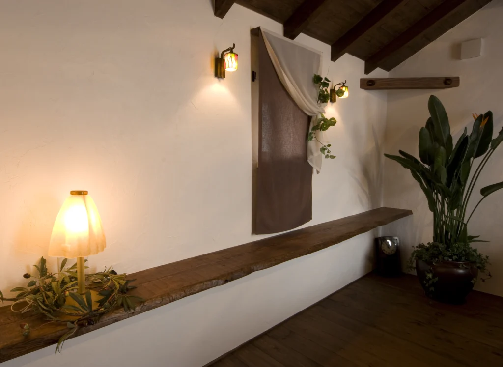 白い塗り壁に沿って設けられた、自然の形状を活かした耳付きの木製造作カウンター。ステンドグラス風の照明やアンティークランプが空間を彩る、アンティクのA邸のディスプレイスペース