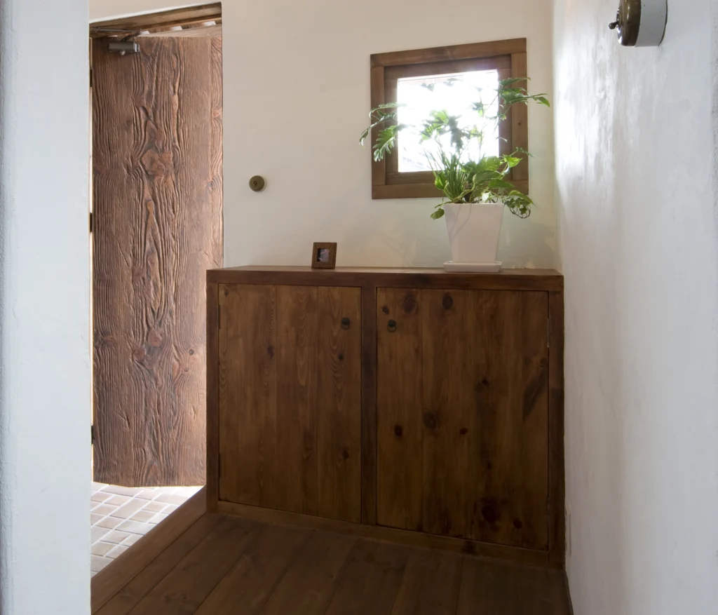 テラコッタ風タイルが敷かれた玄関土間と、無垢材で作られた造作の下駄箱(シューズボックス)。アンティクのA邸の、小窓からの光が差し込む明るい玄関スペース