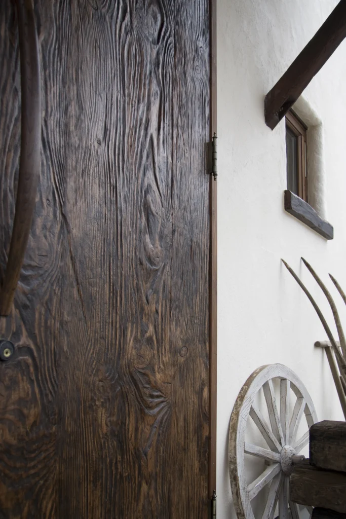 深い木目と使い込まれたような質感が魅力的な、アンティクのA邸の木製玄関ドア。アンティークの蝶番や傍らに置かれた古い車輪が、より一層世界観を引き立てている