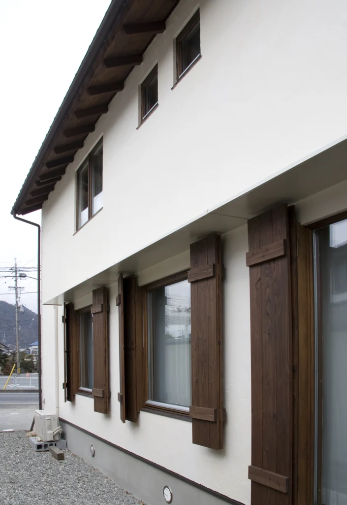 白い塗り壁に木製の鎧戸(雨戸)がアクセントになった、アンティクのA邸の外観。軒天まで木で仕上げられた、細部までこだわりのあるデザイン