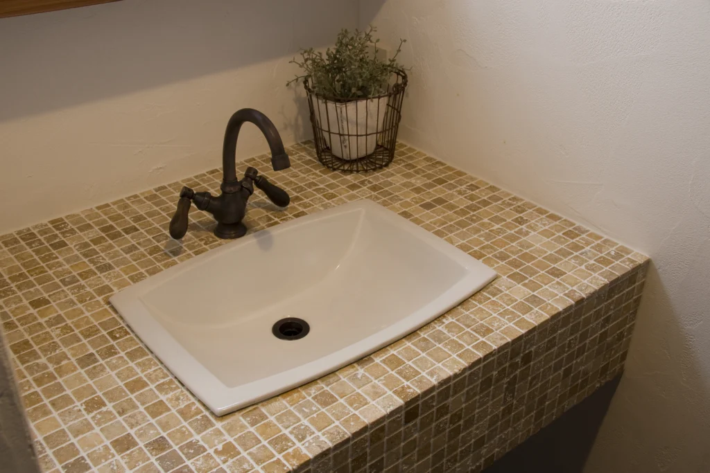 ベージュ系のモザイクタイル天板とアンティーク調のブロンズ水栓が可愛らしい、アンティクのA邸の造作洗面台。コンパクトながらも細部までこだわったデザイン